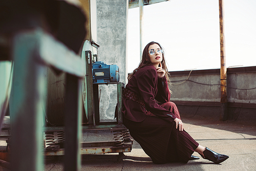 attractive elegant girl posing in trendy burgundy suit and sunglasses on urban roof