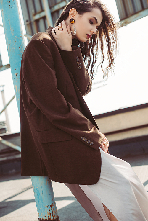 stylish girl posing in silk dress and brown jacket on roof