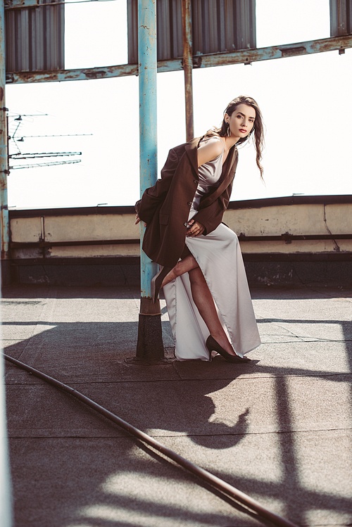 fashionable elegant girl posing in silk dress and brown jacket on roof