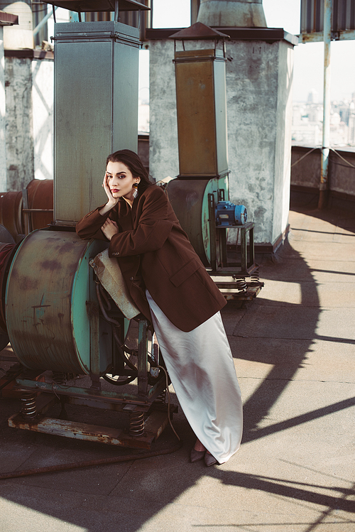 fashionable elegant girl posing in silk dress and brown jacket on roof