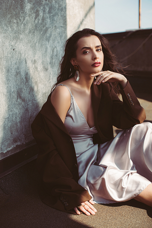 stylish elegant woman posing in silk dress and brown jacket on roof