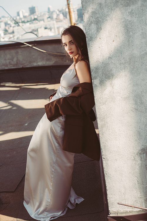 young woman posing in silk dress and brown jacket on roof