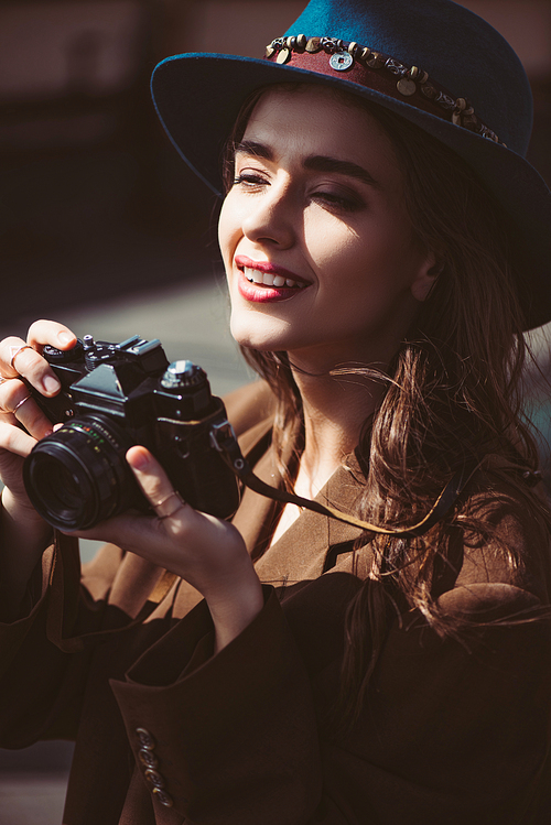 smiling woman in hat taking photos on vintage photo camera on roof