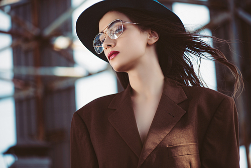 stylish elegant woman posing in hat, eyeglasses and brown jacket on roof