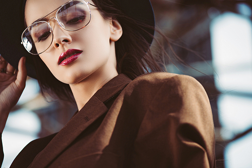 elegant young woman posing in hat, eyeglasses and brown jacket on roof