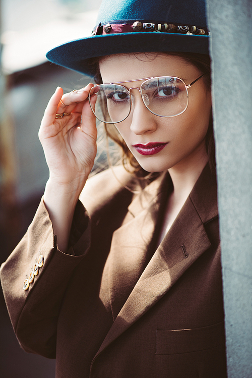 fashionable elegant woman posing in hat, eyeglasses and brown jacket on roof