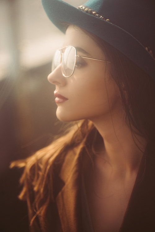 beautiful elegant woman posing in hat, eyeglasses and brown jacket on roof