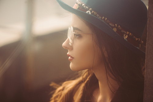 attractive elegant woman posing in hat, eyeglasses and brown jacket on roof