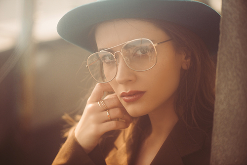 fashionable woman posing in hat, eyeglasses and brown jacket on roof