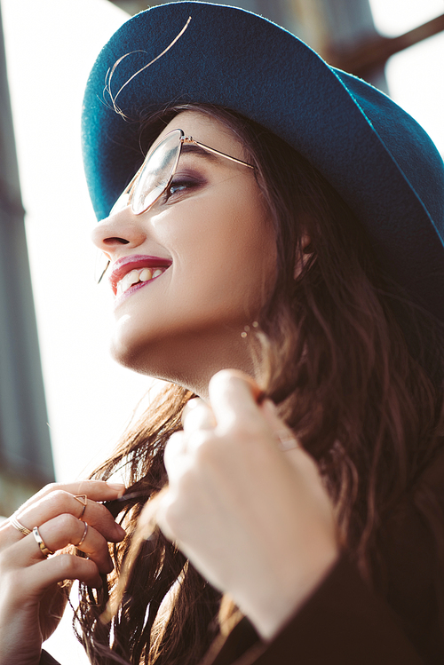 happy stylish girl posing in eyeglasses and hat on urban roof