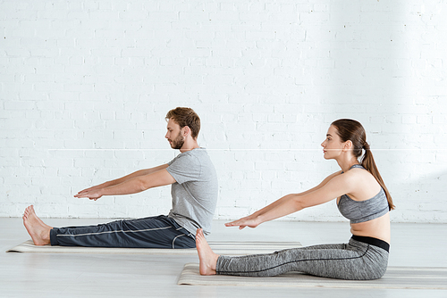 side view of man and woman practicing yoga in seated forward bend pose