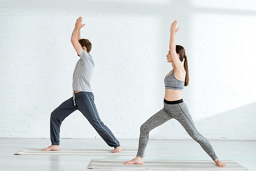 side view of young man and woman practicing yoga in warrior I pose