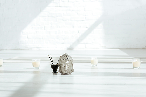 decorative buddha head near aromatic sticks and candles on white floor
