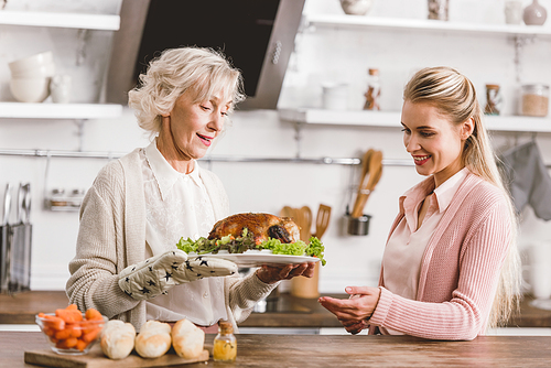 smiling mother and daughter holding plate with tasty turkey in Thanksgiving day
