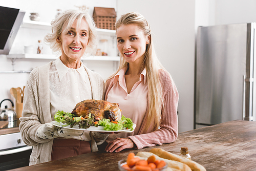 smiling mother and daughter holding plate with tasty turkey in Thanksgiving day