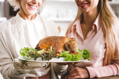 cropped view of smiling mother and daughter holding plate with tasty turkey in Thanksgiving day