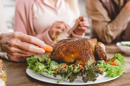 cropped view of woman putting carrot to plate with tasty turkey in Thanksgiving day