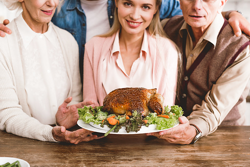 cropped view of smiling family members holding plate with tasty turkey in Thanksgiving day