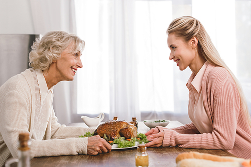 side view of smiling mother and daughter holding plate with turkey in Thanksgiving day