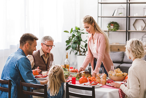 family sitting at table and mother holding plate with turkey in Thanksgiving day