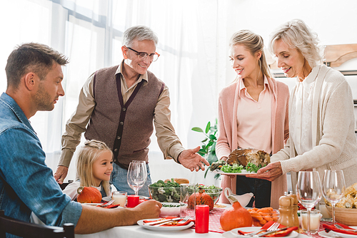 family members sitting at table and holding plate with turkey in Thanksgiving day