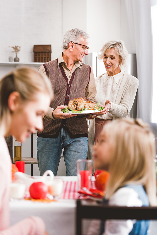 selective focus of family grandparents holding plate with turkey in Thanksgiving day