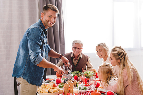 family members sitting at table and father cutting tasty turkey in Thanksgiving day