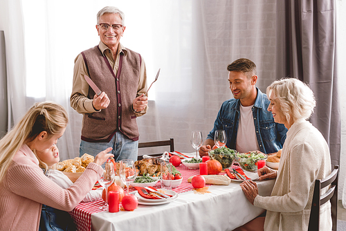 family members sitting at table and grandfather holding cutlery in Thanksgiving day