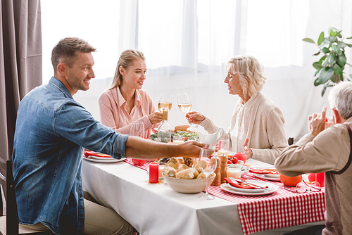 smiling family members sitting at table and clinking with wine glasses in Thanksgiving day