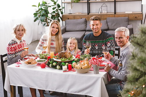smiling family members sitting at table and holding wine glasses in Christmas