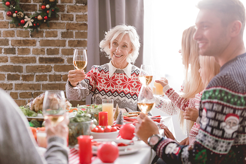 selective focus of family members sitting at table and holding wine glasses in Christmas
