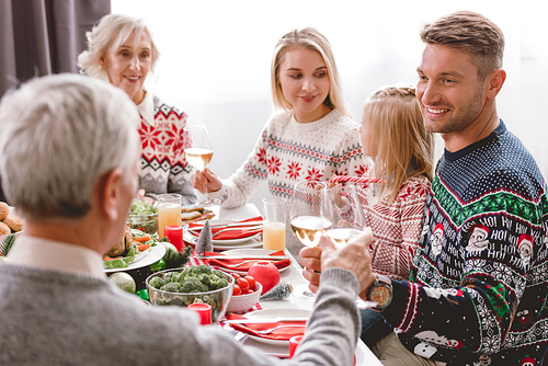 family members sitting at table and clinking with wine glasses in Christmas