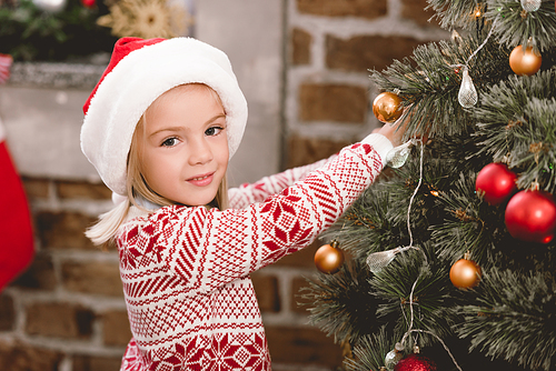 cute kid in santa hat and sweater decorating christmas tree