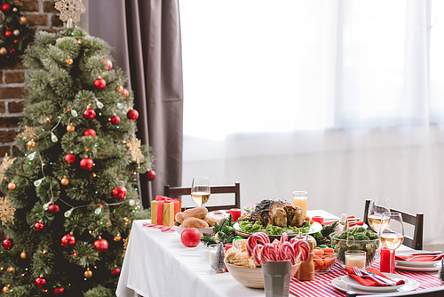 plate with tasty turkey, corn, candy canes, candles, gift and wine glasses on table and christmas tree