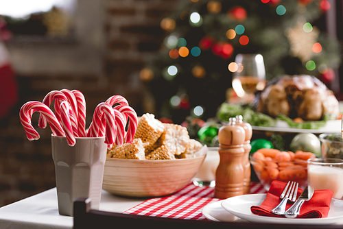 selective focus of candy canes, corn, plates and cutlery on table in christmas