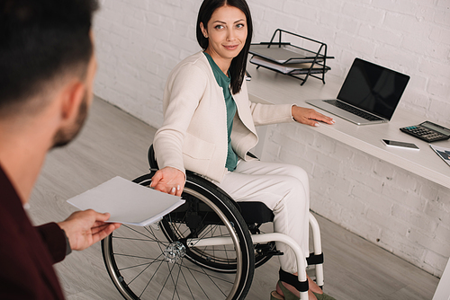 cropped view of manager giving documents to disabled businesswoman in office