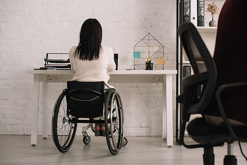 back view of disabled businesswoman sitting at workplace in wheelchair