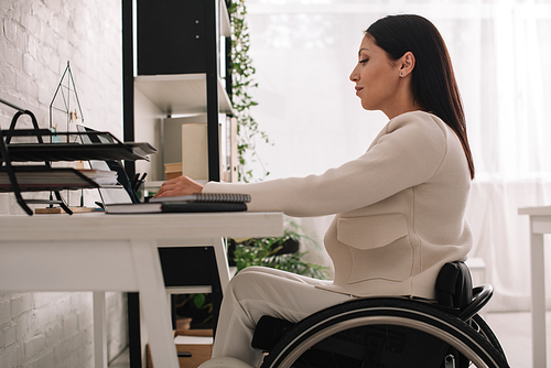 attractive disabled businesswoman using laptop while sitting in wheelchair at workplace