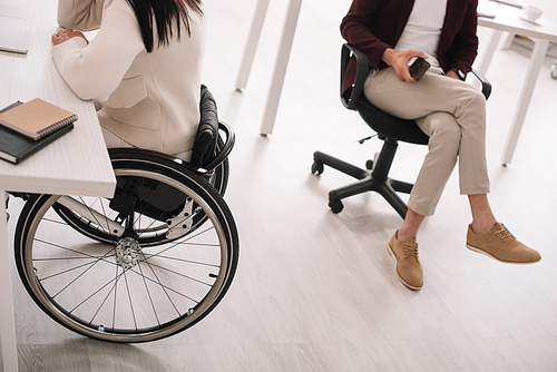 cropped view of businesswoman in wheelchair near business partner in office