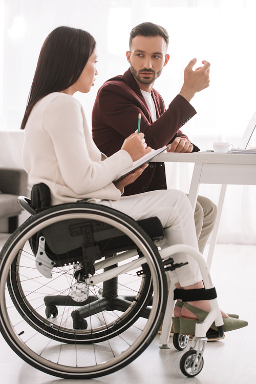 disabled businesswoman holding pencil and notebook while talking with business partner in office