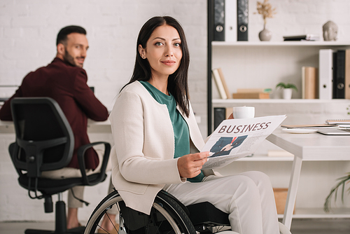 selective positive disabled businesswoman holding newspaper and  while sitting near handsome colleague in office