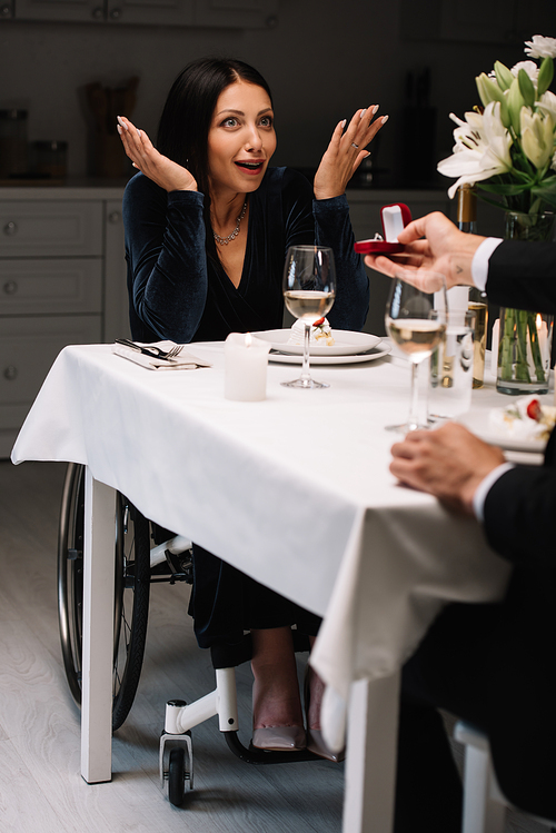 cropped view of man making wedding proposal to happy, surprised disabled girfriend during romantic evening