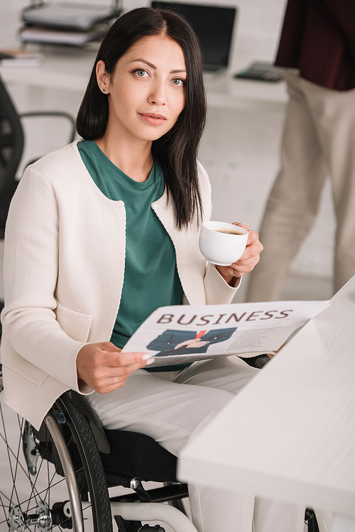 attractive disabled businesswoman holding coffee cup and newspaper while 