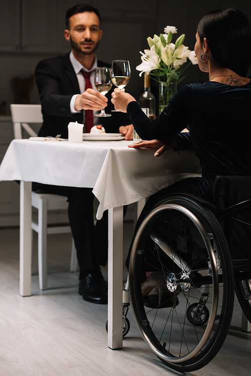back view of disabled young woman clinking glasses of white wine with boyfriend during romantic dinner