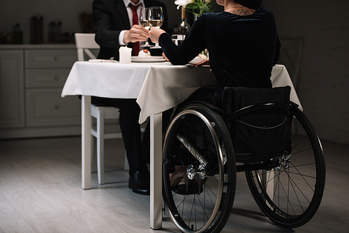 partial view of young woman in wheelchair clinking glasses of white wine with boyfriend during romantic dinner