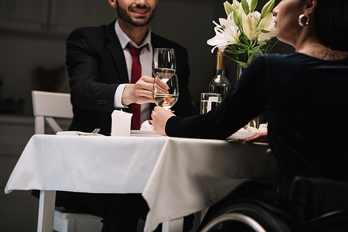 cropped view of disabled young woman clinking glasses of red wine smiling boyfriend during romantic dinner