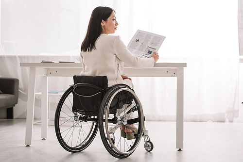 young disabled businesswoman holding newspaper while sitting in wheelchair at workplace