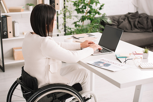 young disabled businesswoman using laptop while sitting in wheelchair at workplace