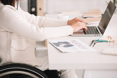 cropped view of disabled businesswoman typing on laptop while sitting at workplace