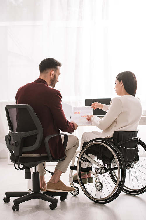 disabled businesswoman in . sitting near colleague and showing documents